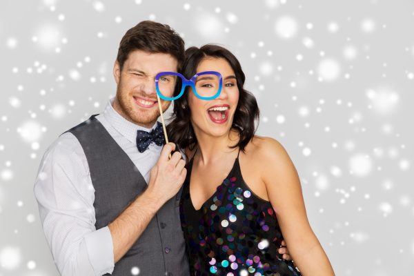 fun and holidays concept - happy couple posing with party props over grey background and snow